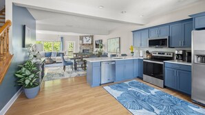 Eine moderne Küche mit blauen Schränken, einer zentralen Kochinsel, Edelstahlgeräten und einem Essbereich mit Holztisch und Stühlen.