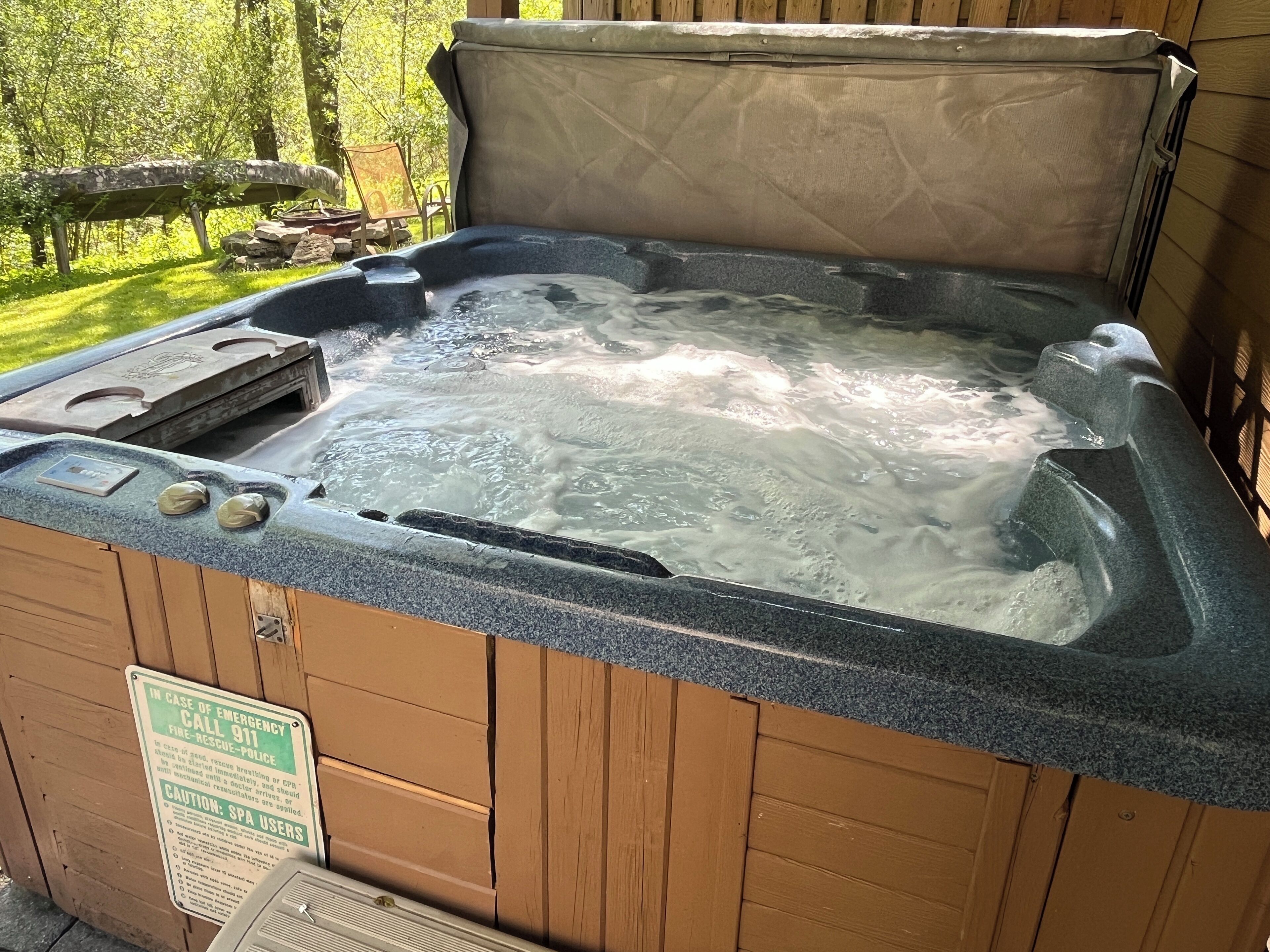 Un bain à remous avec une structure extérieure en bois et une pancarte indiquant les coordonnées à contacter en cas d’urgence.