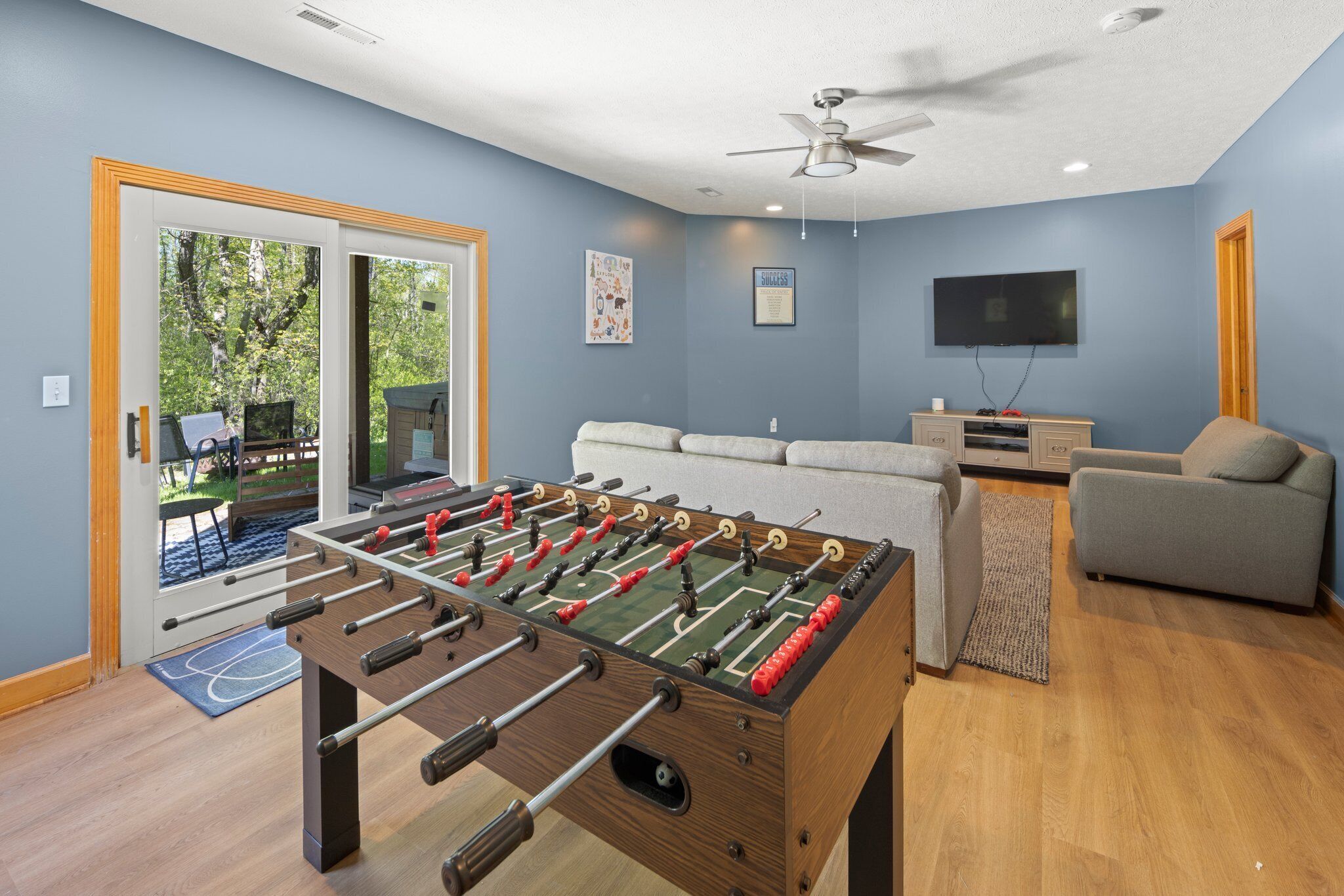 A room with a foosball table, a sofa, a television, and a ceiling fan.