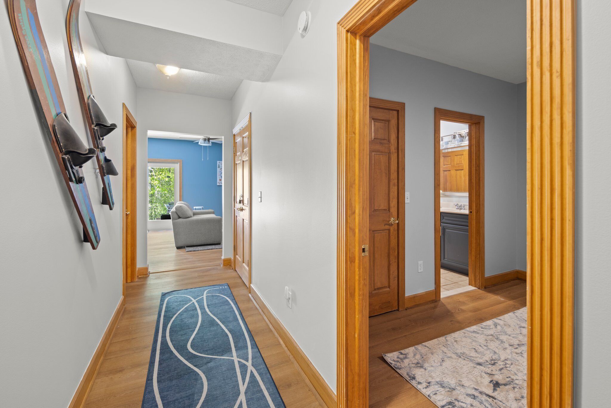 A hallway with wooden flooring, a blue rug, and a wooden door leading to a kitchen.