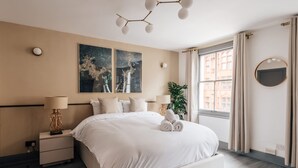 Une chambre moderne avec un grand lit, deux œuvres d’art accrochées au mur, une table de chevet avec une lampe et une fenêtre avec des rideaux.