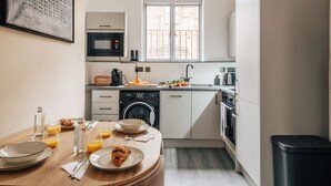 Une cuisine moderne avec un coin repas, comprenant une table mise pour le petit-déjeuner, un lave-linge et une fenêtre donnant sur l’extérieur.
