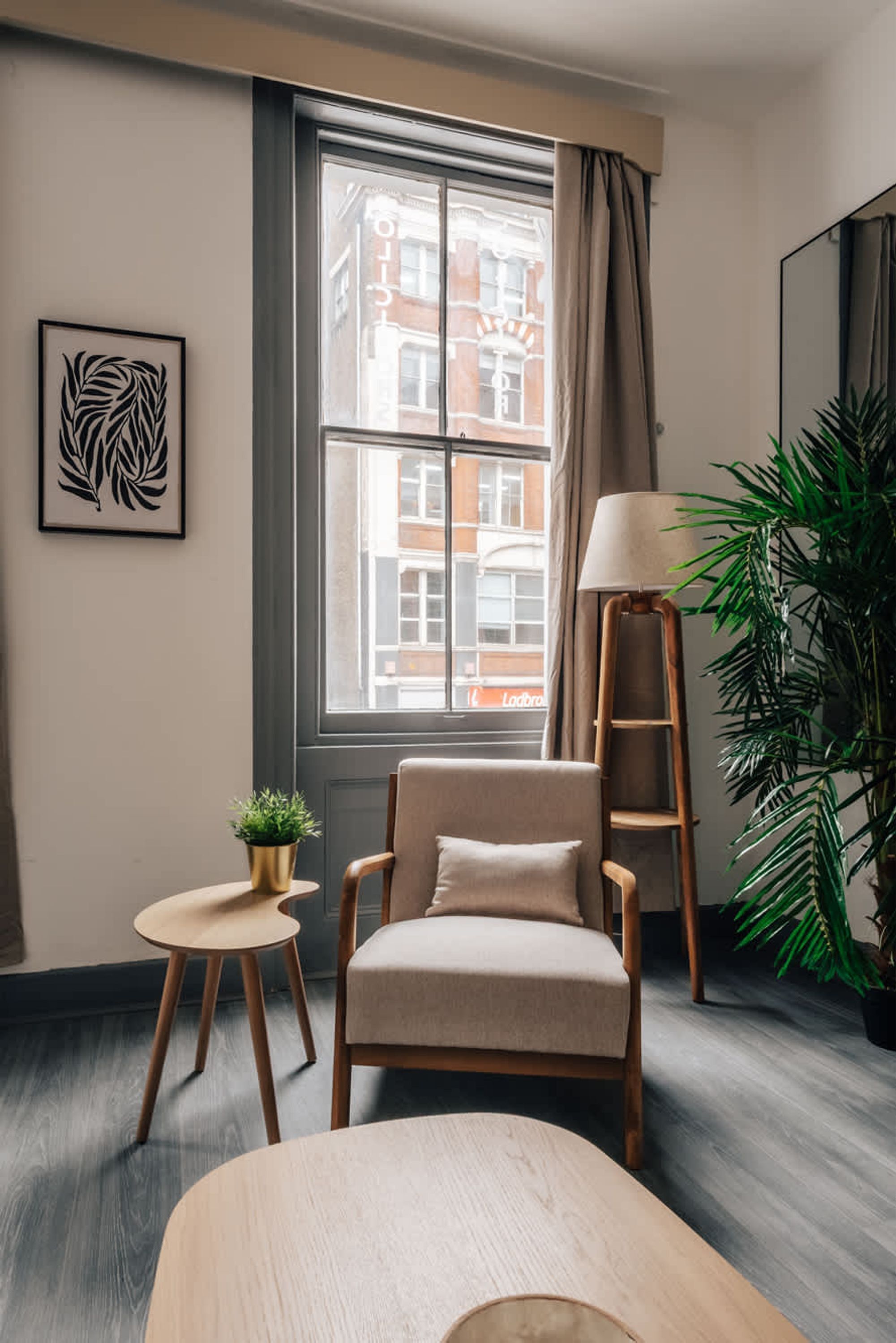 Een moderne kamer met een groot raam, een stoel, een klein tafeltje, een vloerlamp en een potplant.