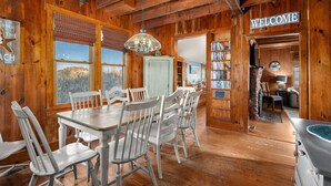 Un interior de madera con una mesa y sillas de comedor, un letrero que dice 'WELCOME' y una vista por la ventana.