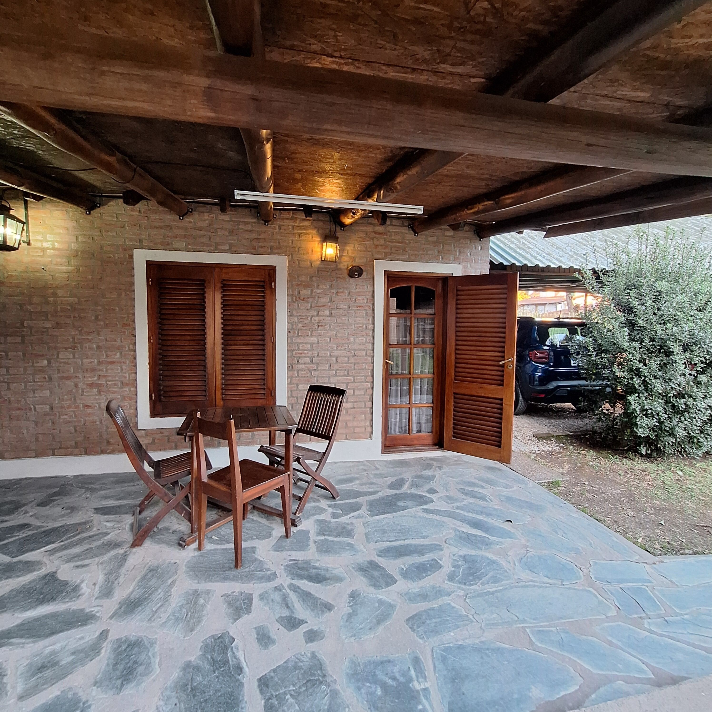 Une terrasse en pierre avec une table et des chaises en bois, un mur en briques et une porte en bois.