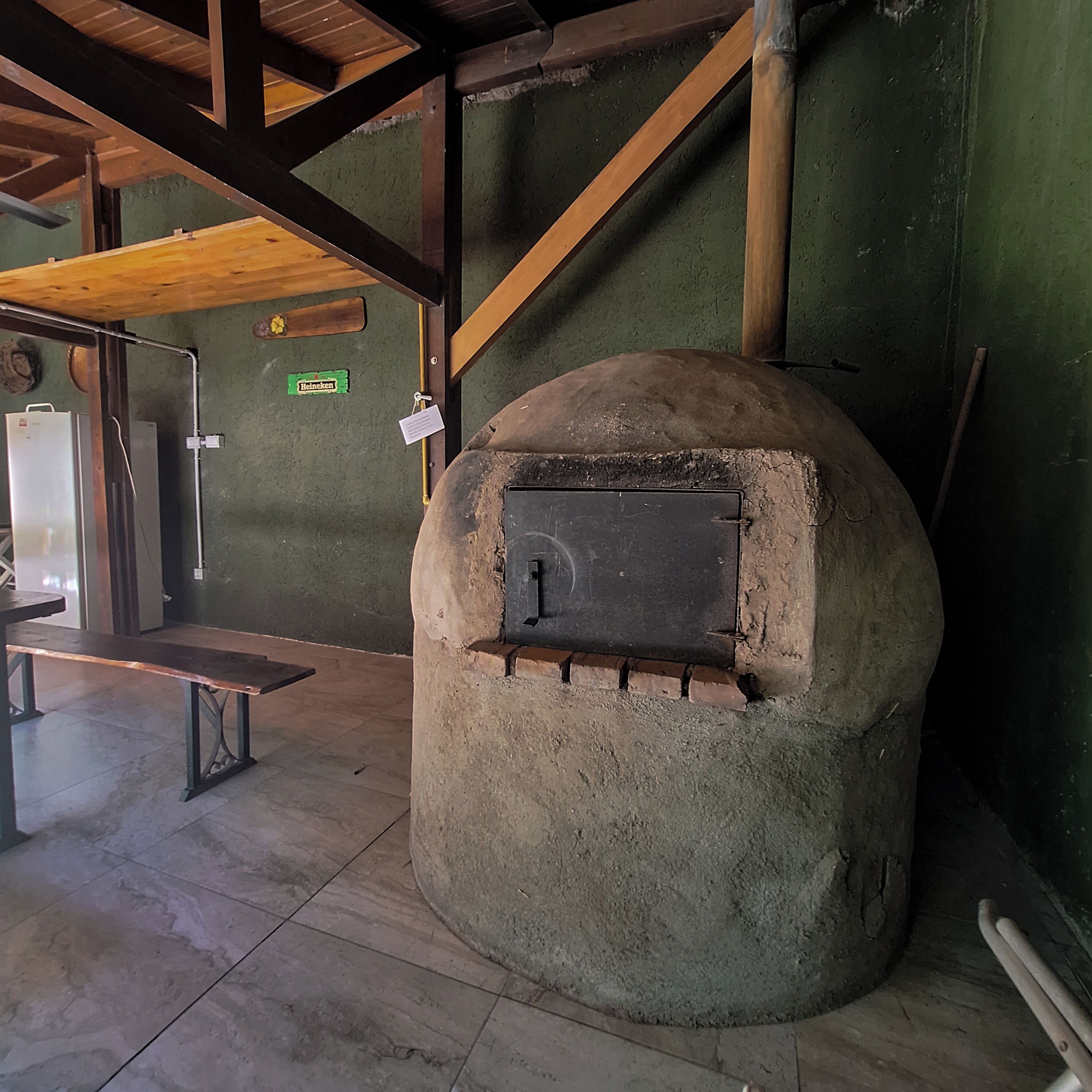 Un espacio interior con un horno de piedra, vigas de madera, un banco y un letrero que indica una marca Heineken.