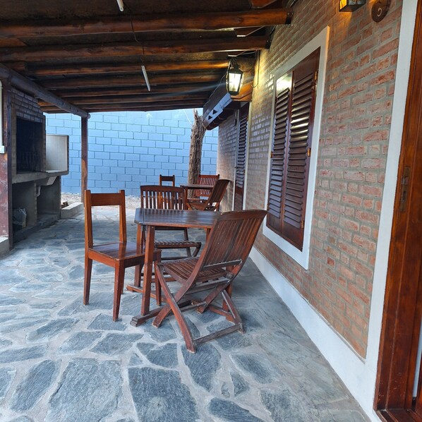 An outdoor patio with stone flooring, wooden furniture, and a brick wall. - Hostal La Merced (Villa General Belgrano)
