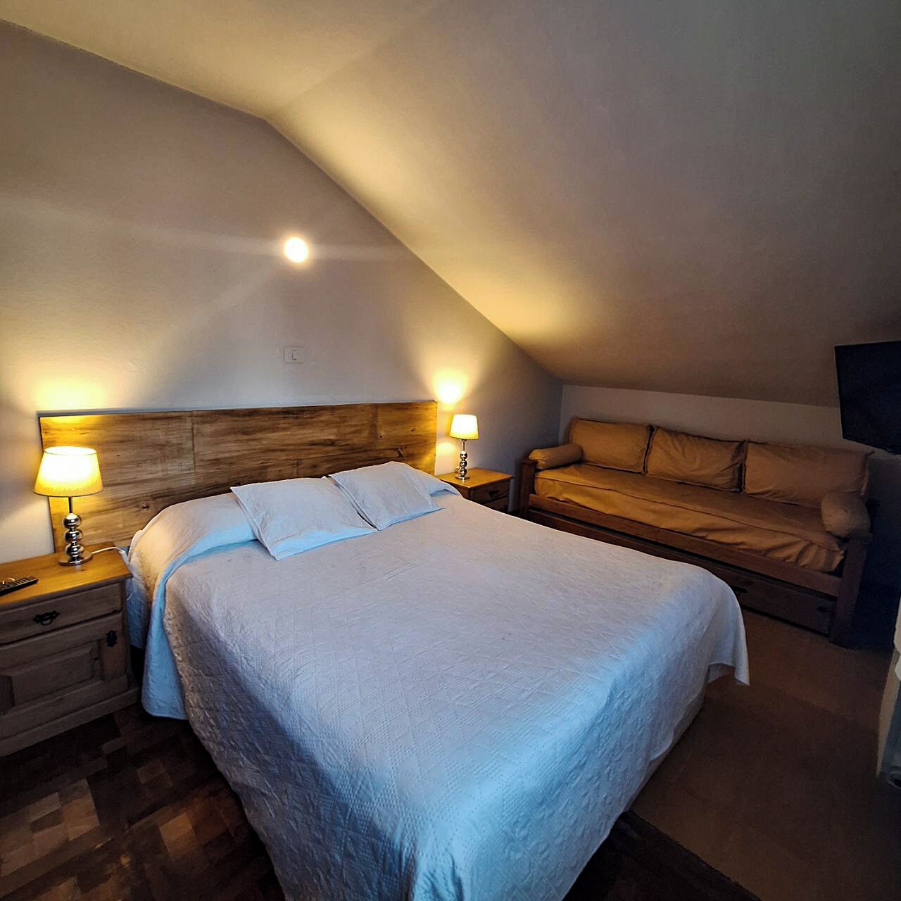 Een slaapkamer met een groot bed, een kleinere bank, twee bedlampen en een houten hoofdeinde.