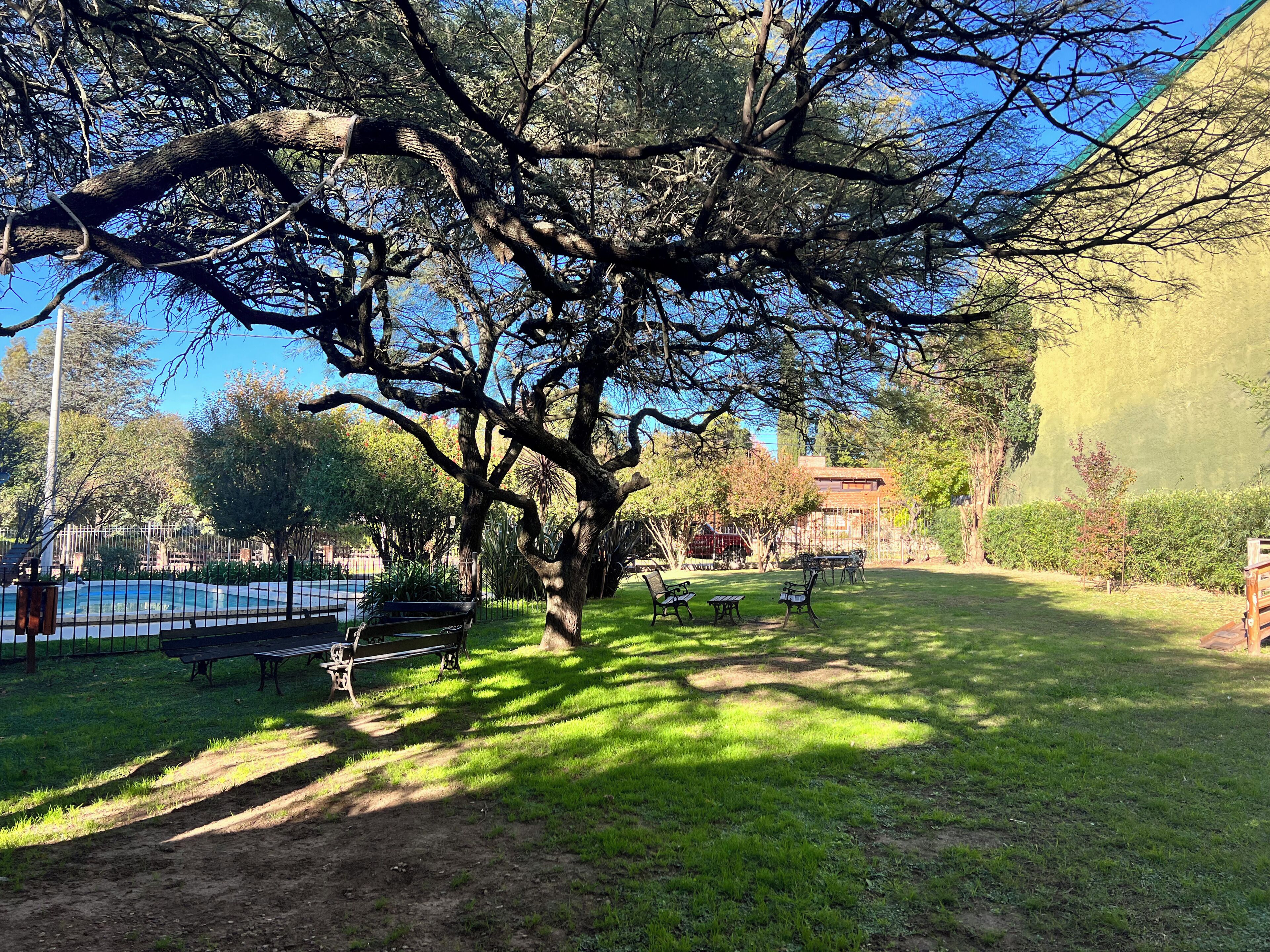 Un parque con un árbol grande, bancos y un área cercada.