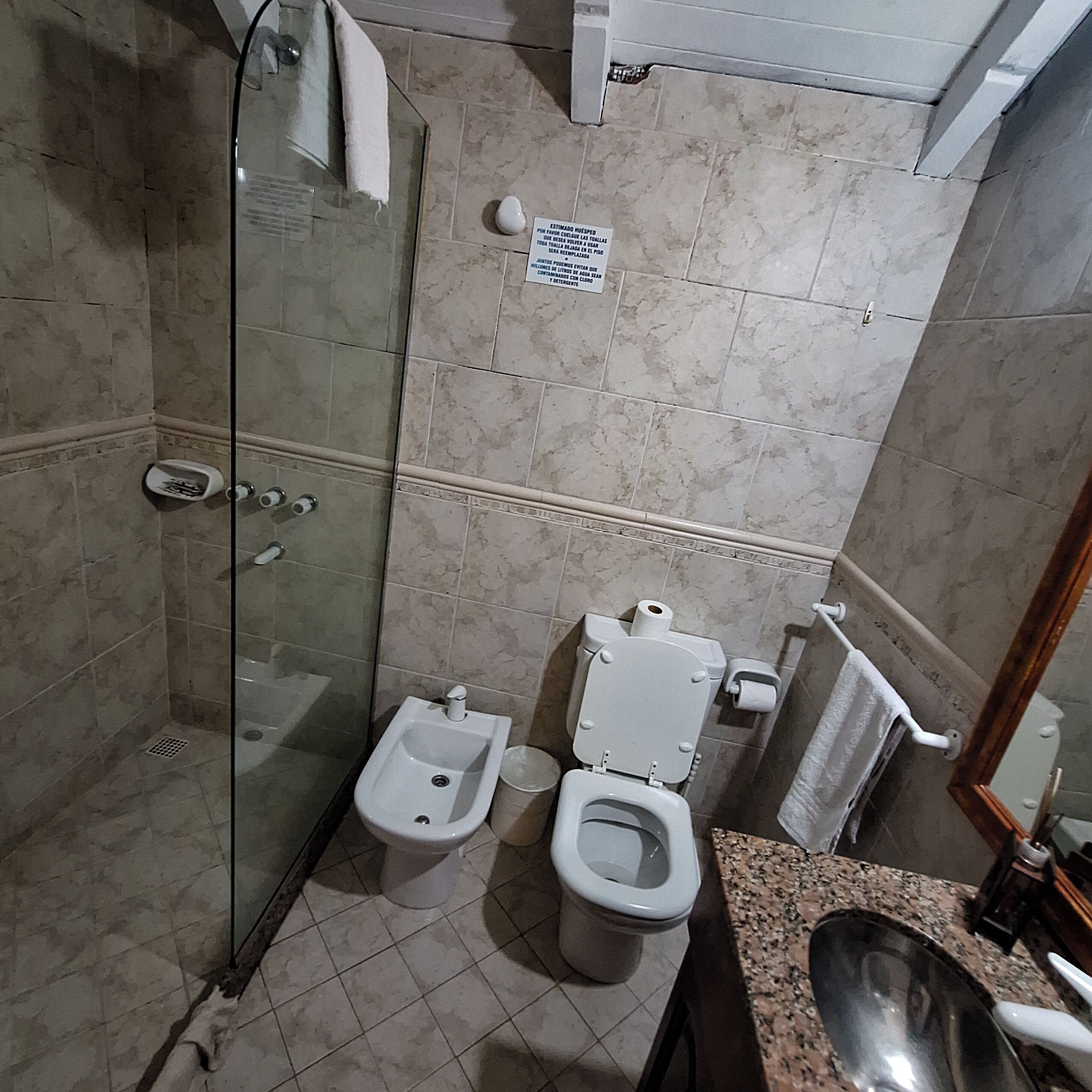 Un baño con ducha acristalada, un bidé, un inodoro y una encimera de granito con lavabo.