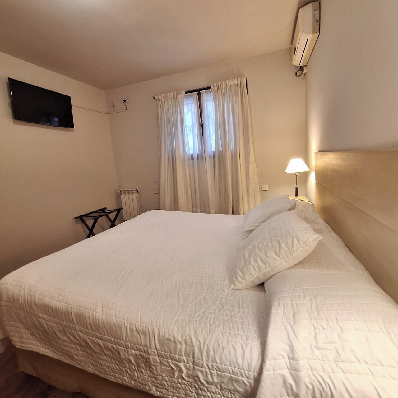 Een slaapkamer met een bed, gordijnen, een televisie, een lamp en een radiator.