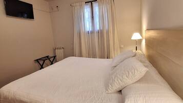 Een slaapkamer met een bed, gordijnen, een televisie, een lamp en een radiator.