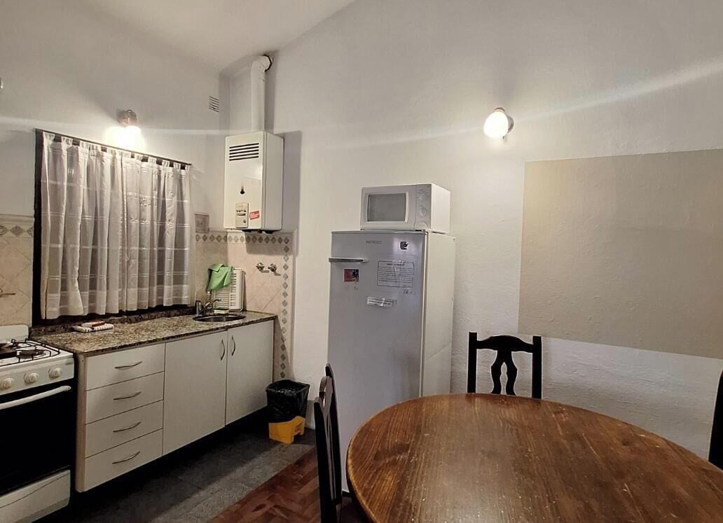 Una cocina compacta con estufa, microondas, refrigerador y una mesa de comedor.