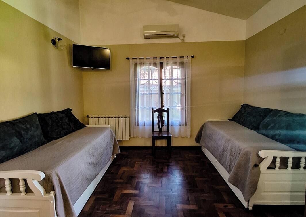 A room with two single beds, a television mounted on the wall, a window with curtains, and a radiator.