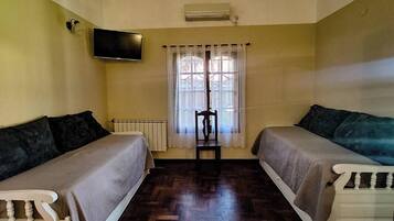 A room with two single beds, a television mounted on the wall, a window with curtains, and a radiator.