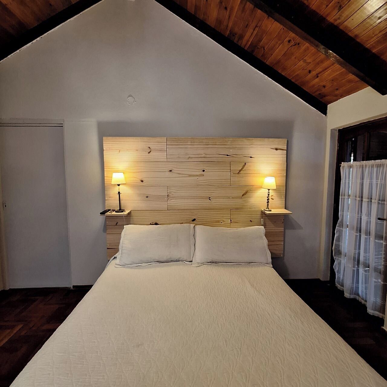 A bedroom with a wooden headboard, two bedside lamps, a bed with white bedding, and a wooden ceiling.