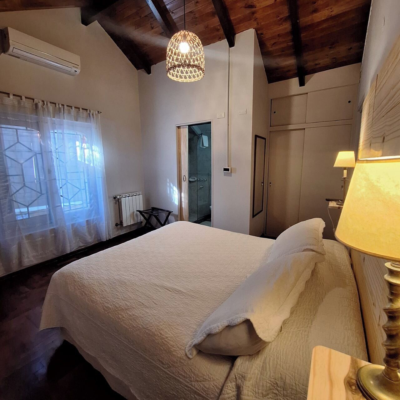 Une chambre à coucher comprenant un lit, un luminaire suspendu, un radiateur et une porte donnant sur une salle de bain.