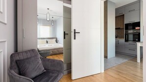 A modern interior with a bed, a gray sofa, a white door, and a kitchen area. - Nadmotławie Chic Apartment (Gdańsk)