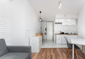 Une cuisine moderne avec des meubles blancs, un plan de travail en bois et un coin repas comprenant un canapé gris et une table.