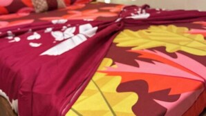 Un lit avec une couvre-lit à motifs rouges et jaunes, une tête de lit en bois et un oreiller blanc.