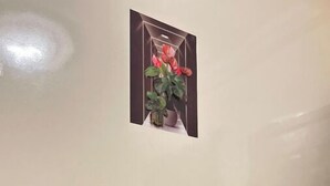 Une petite pièce avec un bureau en bois, une chaise, un tableau représentant des fleurs accroché au mur et une bouteille d’eau.