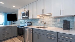 A modern kitchen with stainless steel appliances, grey cabinets, and a tiled backsplash. - Fountainhead-Oceanfront Retreat w/ Expansive Private Balcony (Ocean City)