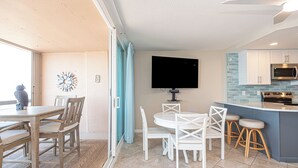 A modern kitchen with a flat-screen TV, a dining area with wooden chairs, and a blue accent wall. - Fountainhead-Oceanfront Retreat w/ Expansive Private Balcony (Ocean City)