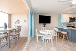 A modern kitchen with a flat-screen TV, a dining area with wooden chairs, and a blue accent wall. - Fountainhead-Oceanfront Retreat w/ Expansive Private Balcony (Ocean City)