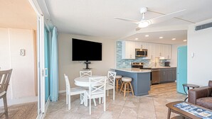 A modern kitchen with a central island, a dining area with white chairs, a flat-screen TV mounted on the wall, and a ceiling fan. - Fountainhead-Oceanfront Retreat w/ Expansive Private Balcony (Ocean City)