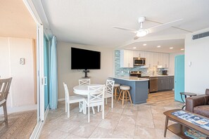 A modern kitchen with a central island, a dining area with white chairs, a flat-screen TV mounted on the wall, and a ceiling fan. - Fountainhead-Oceanfront Retreat w/ Expansive Private Balcony (Ocean City)