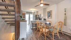 Une cuisine avec un plancher en bois, un coin repas avec des chaises en osier, un ventilateur de plafond et une enseigne indiquant « OCEAN CITY ».