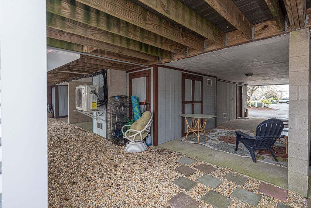 An outdoor covered area with a gravel floor, a chair, a table, and a building with wooden beams.