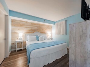 A bedroom with a wooden headboard, a bed with white bedding, a bedside table with a lamp, and a wardrobe. - Roxanne Towers 303 (Myrtle Beach)