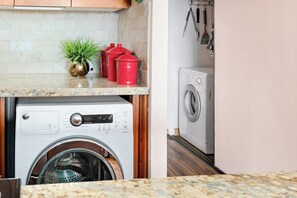 A kitchen with a washing machine, a countertop with a plant, and red containers. - Maui Vista 2310 - Fully Remodeled 1 BR/1 BA Close to Beach (Kihei)