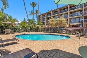 A pool area with lounge chairs and umbrellas, surrounded by palm trees and a multi-story building. - Maui Vista 2310 - Fully Remodeled 1 BR/1 BA Close to Beach (Kihei)