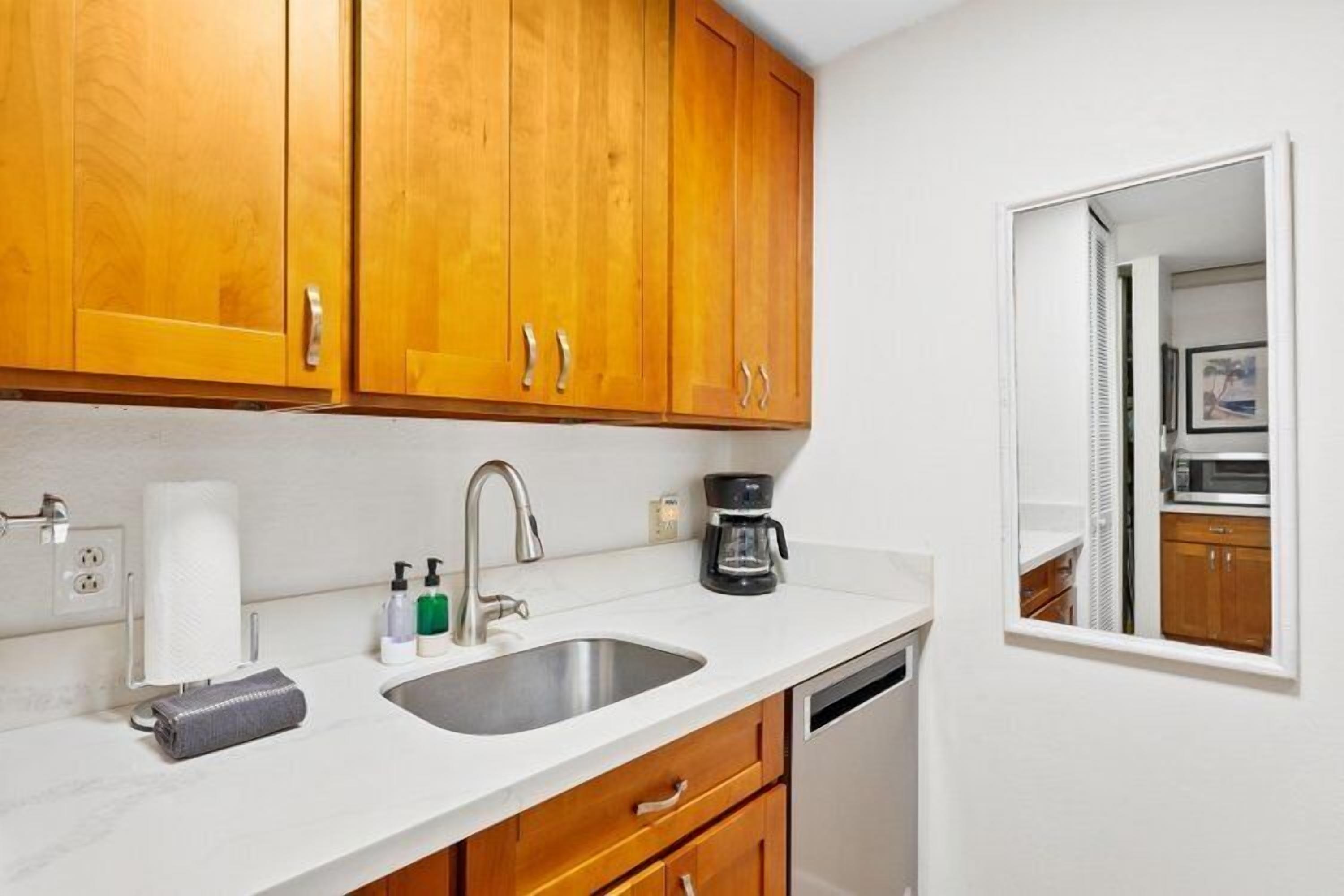 A kitchen with wooden cabinets, a sink, a coffee maker, and a dishwasher.