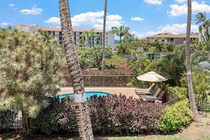 A pool area with lounge chairs and an umbrella, surrounded by palm trees and various plants. - Maui Vista 3212 - Inviting 1 BR/1 BA near Beach (Kihei)