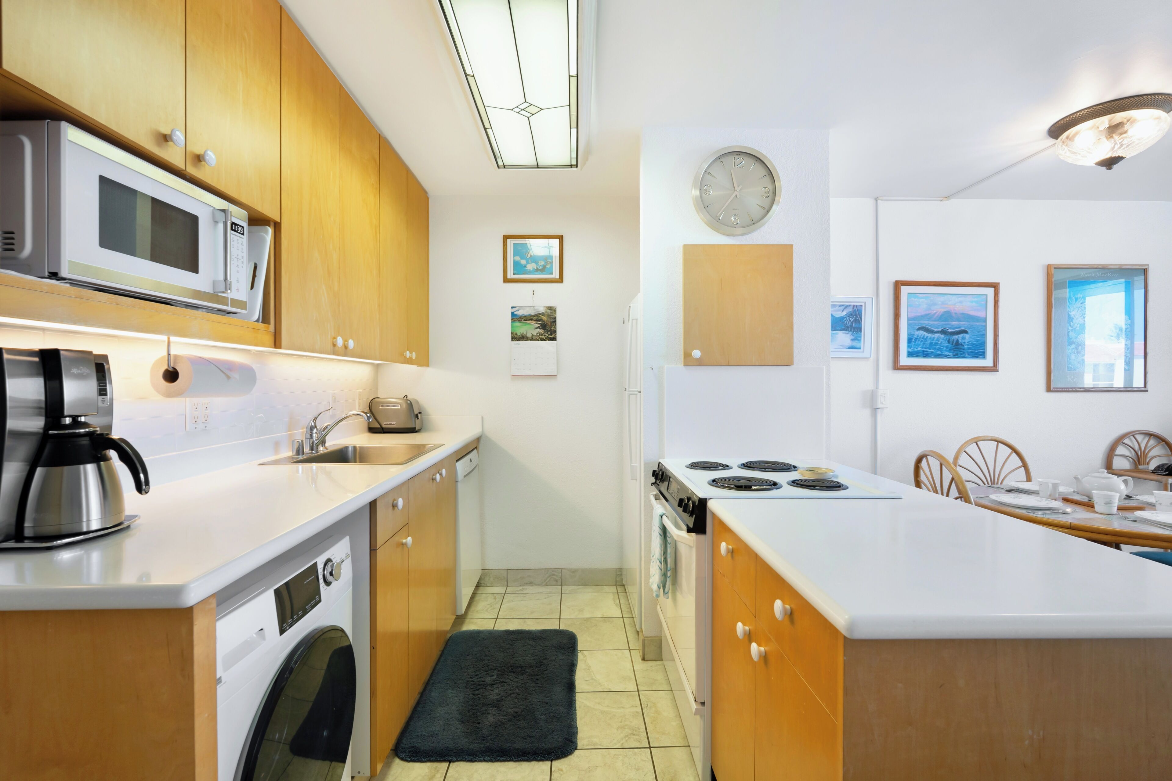 A modern kitchen with wooden cabinets, a built-in microwave, a coffee maker, and a dining area with chairs and a table.