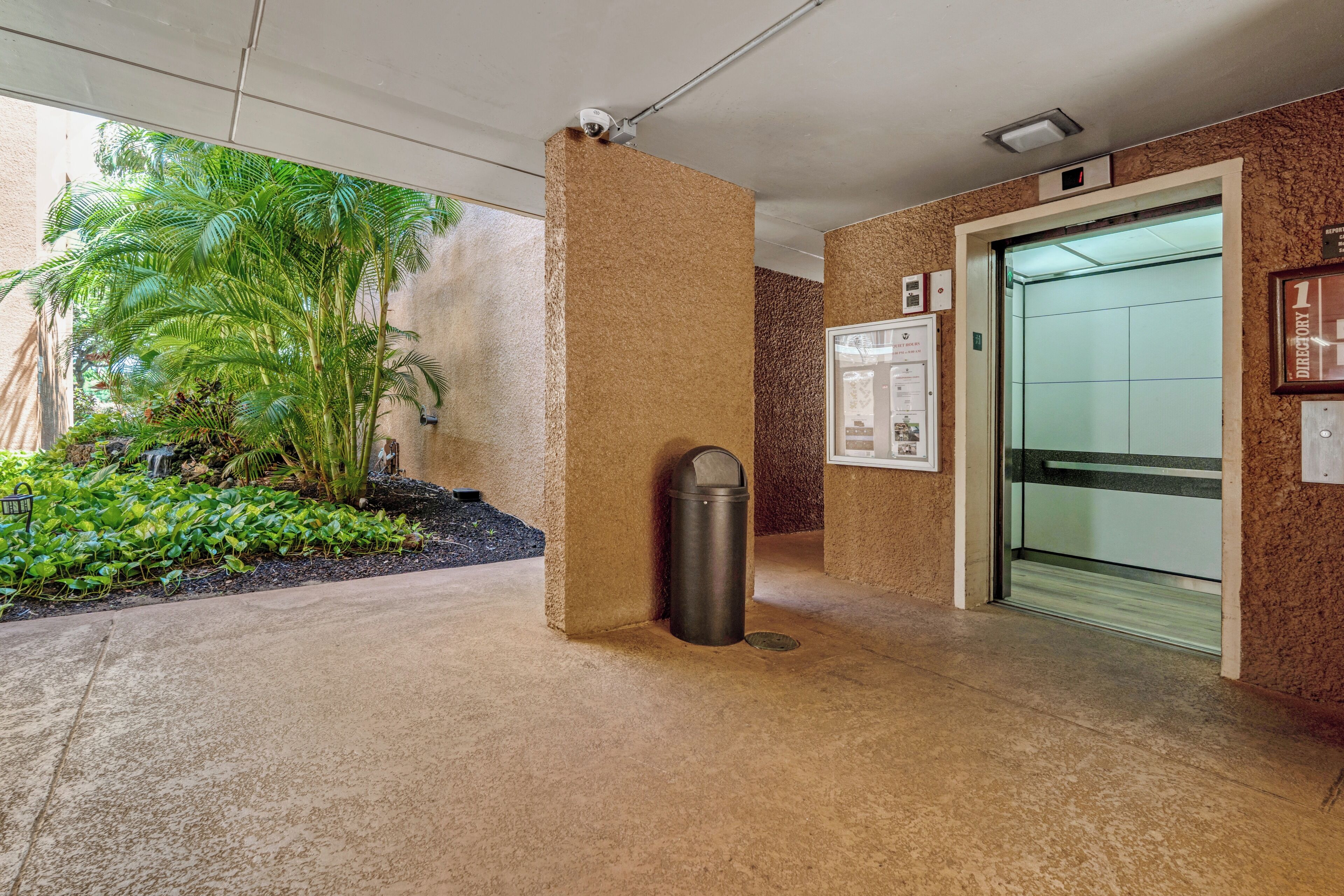 Un espacio interior con piso de concreto, un basurero, una puerta y una cámara de seguridad fijada a la pared.