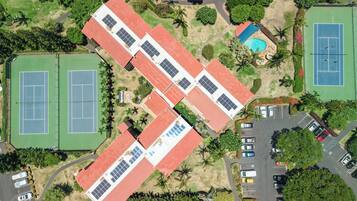 Een luchtbeeld van een sportcomplex met tennisbanen, een zwembad en zonnepanelen op het dak.