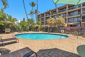 A swimming pool with lounge chairs and umbrellas, surrounded by palm trees and a multi-story building with balconies. - Maui Vista 3312 - Updated & Comfortable 1 BR/1 BA near Beach (Kihei)