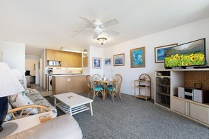 A modern living room with a sofa, a dining table with chairs, a television, and a kitchen area with cabinets and a microwave. - Maui Vista 3312 - Updated & Comfortable 1 BR/1 BA near Beach (Kihei)