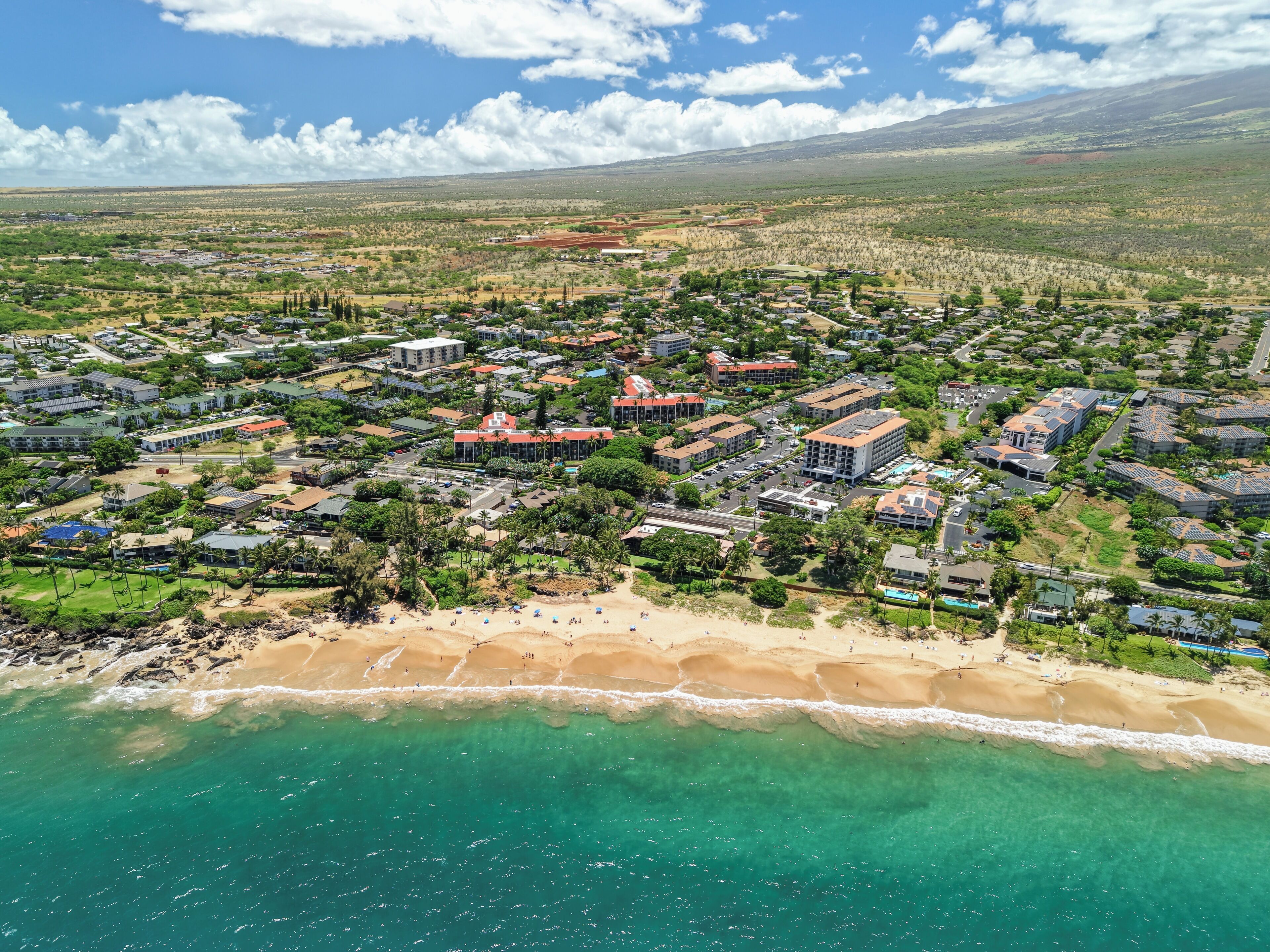 Vue aérienne d’une zone résidentielle côtière, avec des maisons, des routes et une plage.