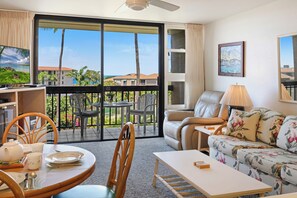 A living room with a sofa, a table, chairs, a balcony with a view of buildings and palm trees. - Maui Vista 3312 - Updated & Comfortable 1 BR/1 BA near Beach (Kihei)