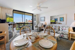 A dining area with a table set for four, a sofa, a chair, and a balcony with a view. - Maui Vista 3312 - Updated & Comfortable 1 BR/1 BA near Beach (Kihei)