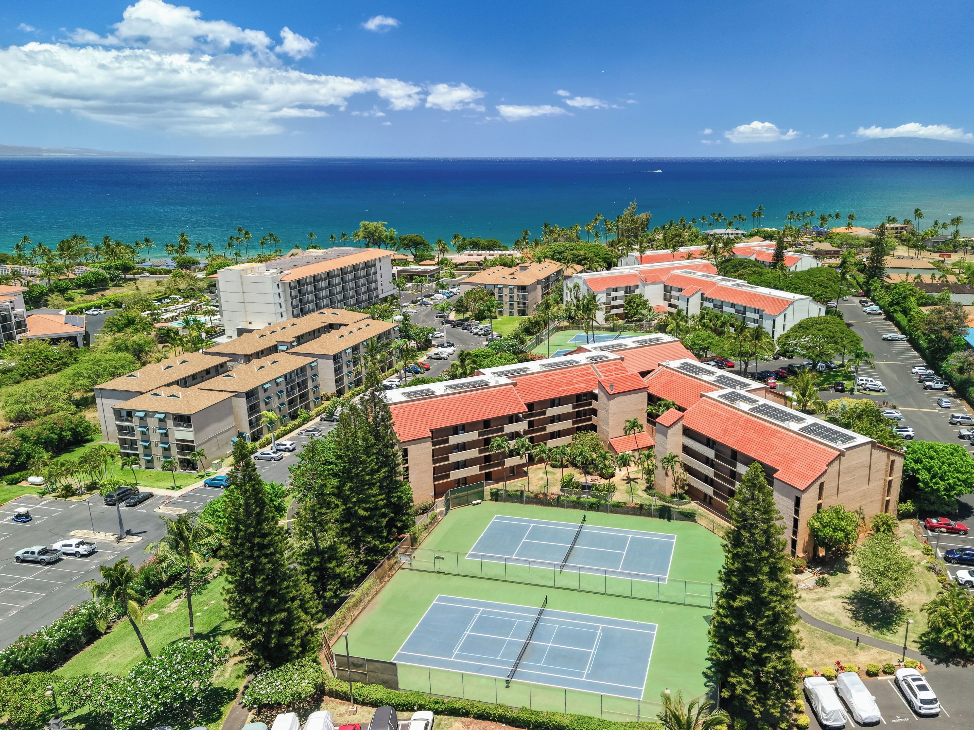 Un complejo turístico con varias construcciones, una cancha de tenis y vistas al océano.