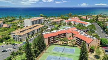 Un complejo turístico con varias construcciones, una cancha de tenis y vistas al océano.