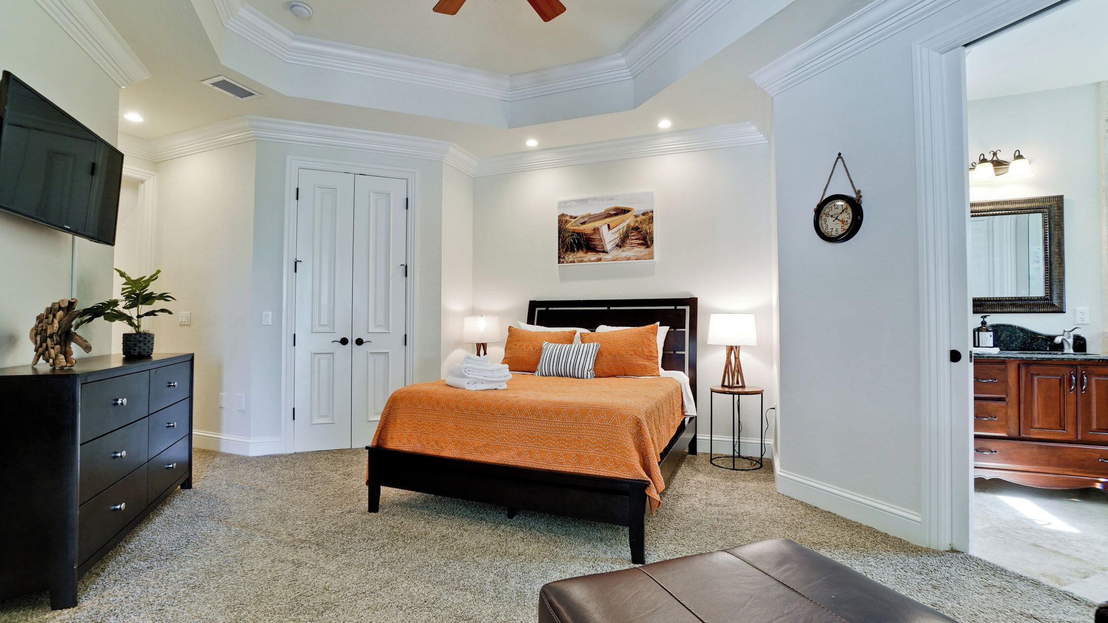 Quarto com cama, penteadeira, mesa de cabeceira, abajur, relógio e um quadro na parede.