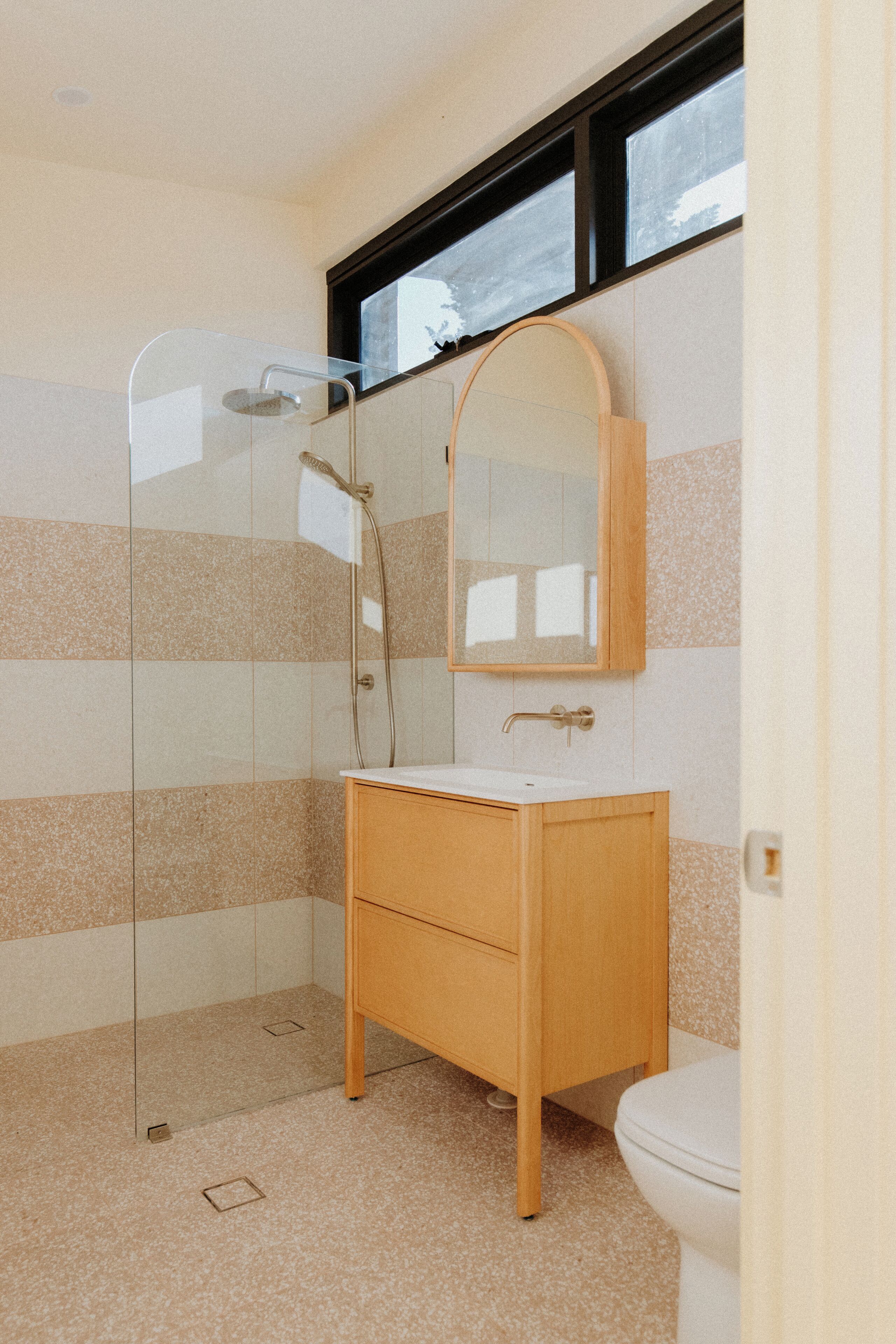 A bathroom with a glass shower enclosure, a wooden vanity, and a mirror above the sink.