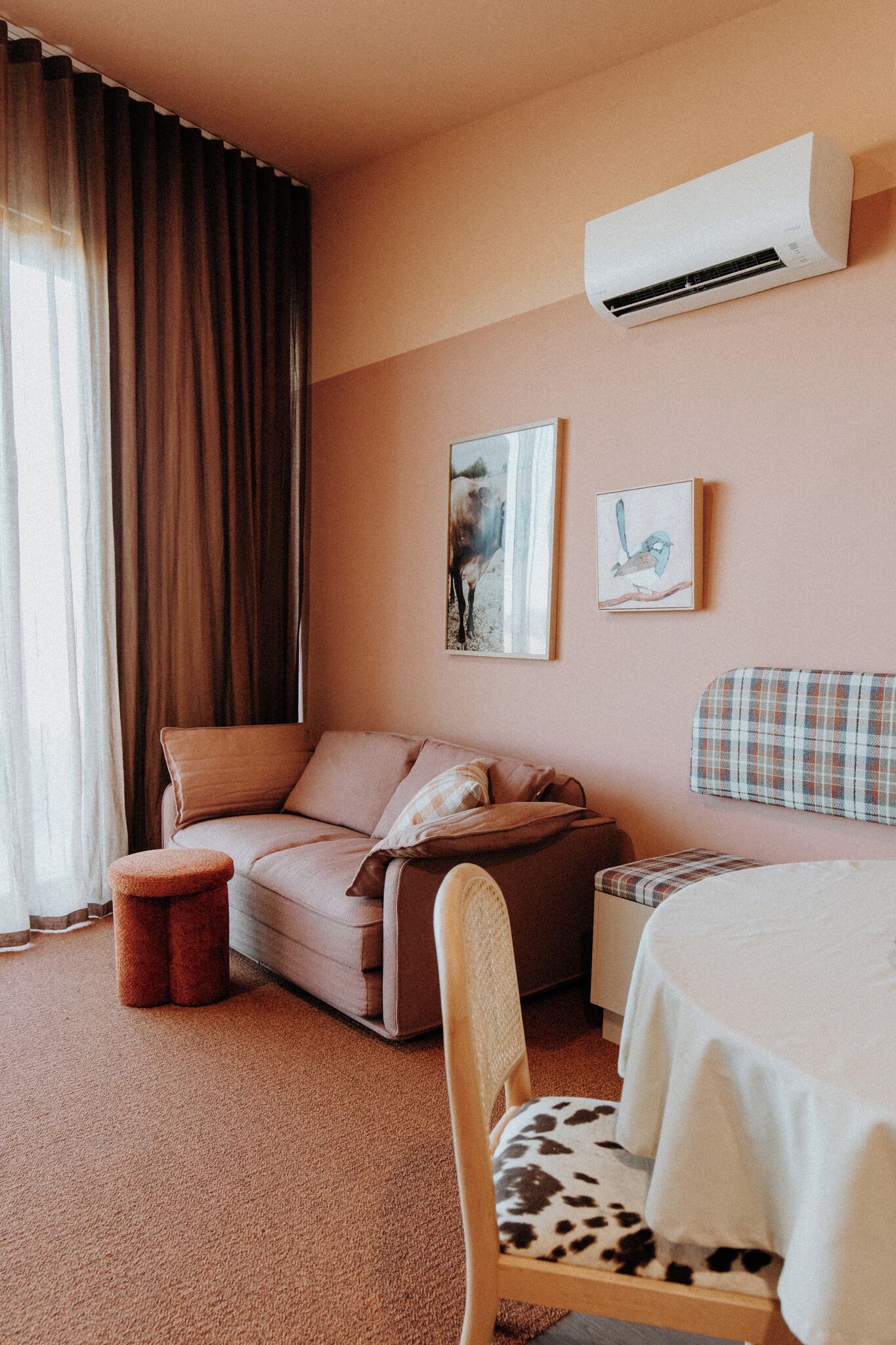A cozy room with a sofa, a chair with a cow print cushion, a small table, and an air conditioning unit on the wall.